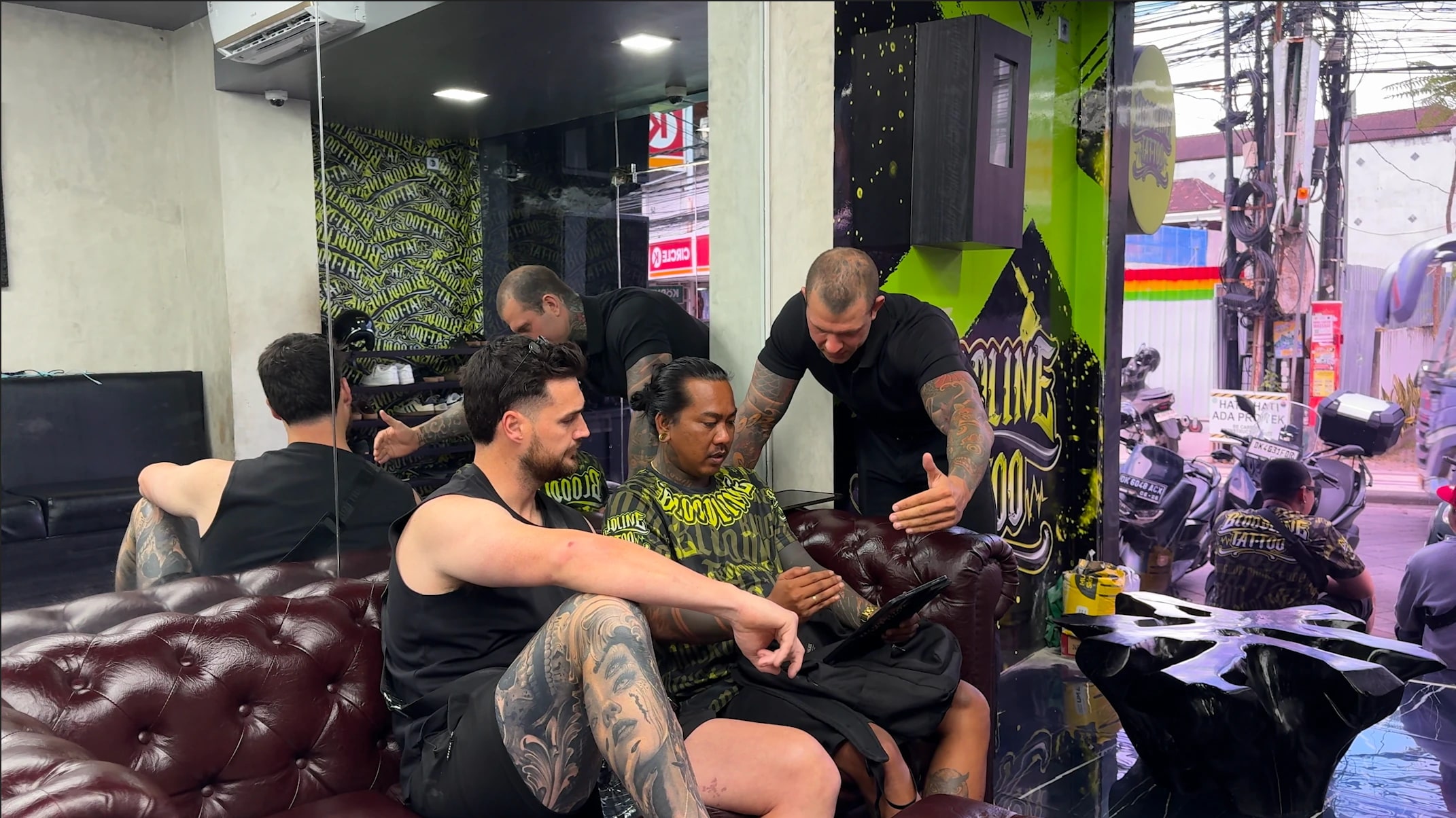 Client and artists reviewing design quality on a tablet beside visible black and grey realism work at Bloodline Tattoo Bali