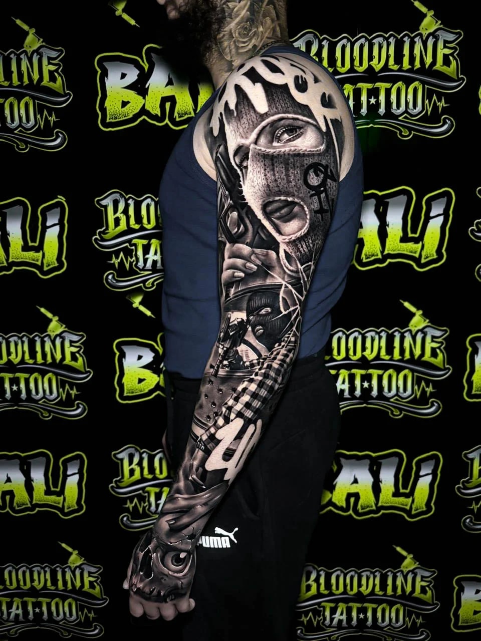 Detailed black and grey Chicano full arm sleeve tattoo featuring a masked woman, pistols, checkerboard patterns, and skull imagery at Bloodline Tattoo Bali.