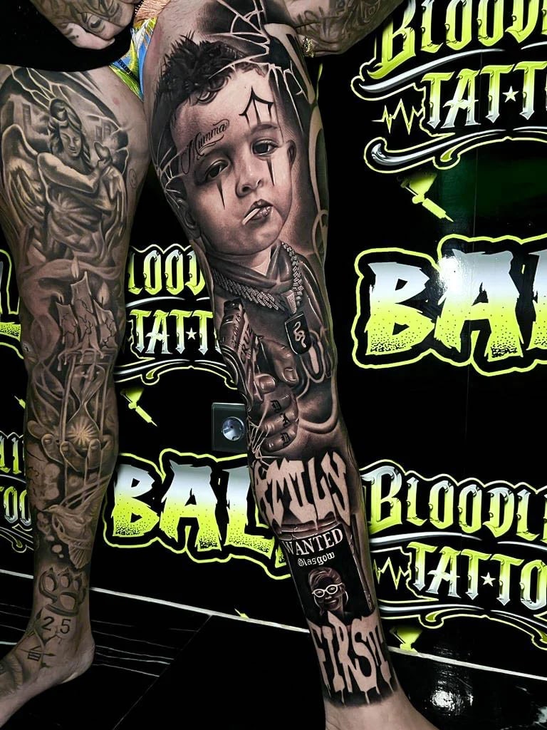 Detailed black and grey Chicano thigh tattoo of a teardrop child portrait with a cigarette, chain necklace, hand sign, and graffiti lettering at Bloodline Tattoo Bali.