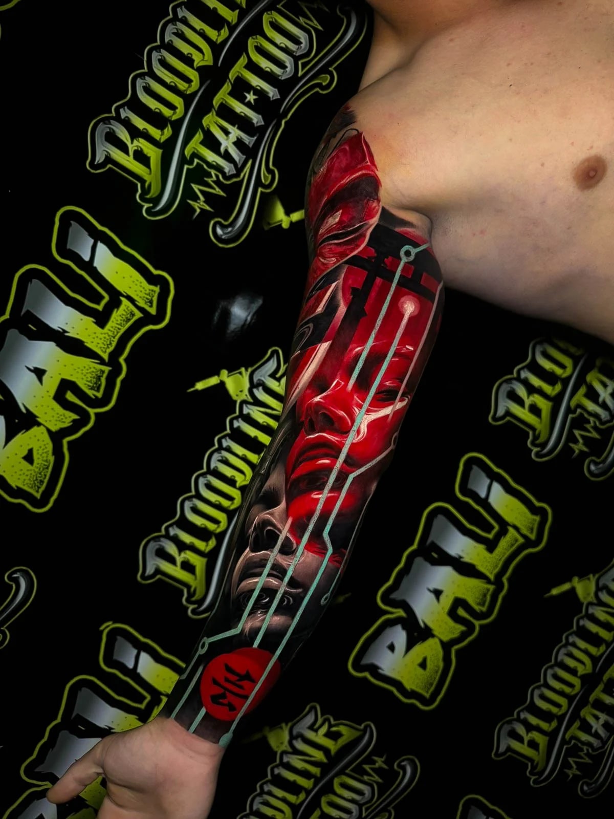 Colour surreal cyberpunk forearm sleeve tattoo with a glossy red face, grayscale portrait, and glowing blue circuit lines at Bloodline Tattoo Bali.