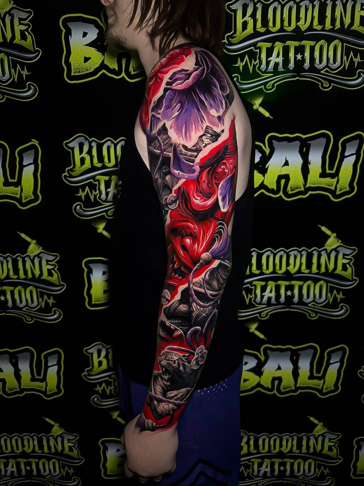 Colour fantasy full arm sleeve tattoo with purple mountain scenery, red demonic faces, and swirling abstract ribbons at Bloodline Tattoo Bali.