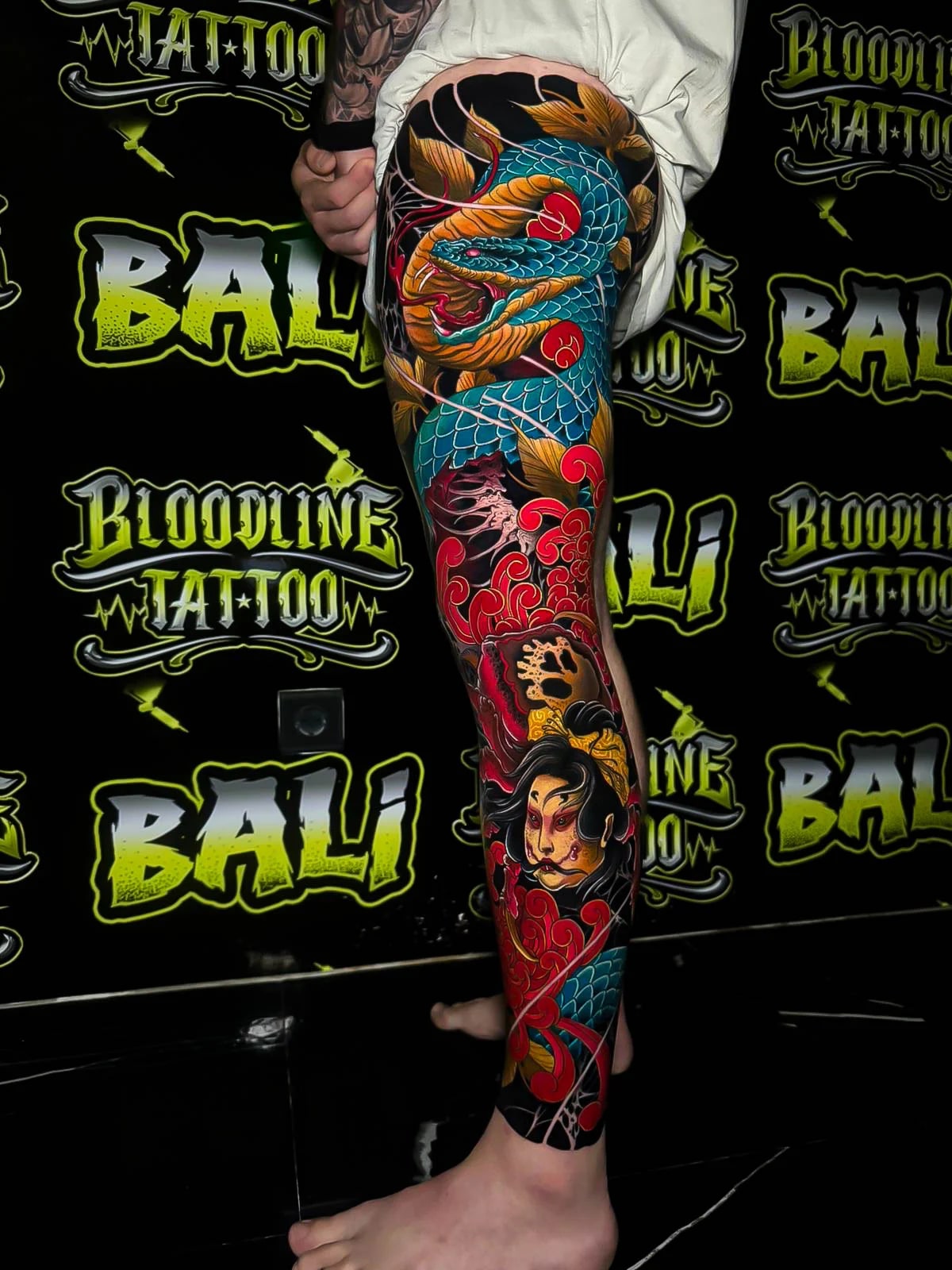 Colour Japanese leg sleeve tattoo with a blue serpent, red cloud swirls, and a geisha portrait in rich traditional tones at Bloodline Tattoo Bali.