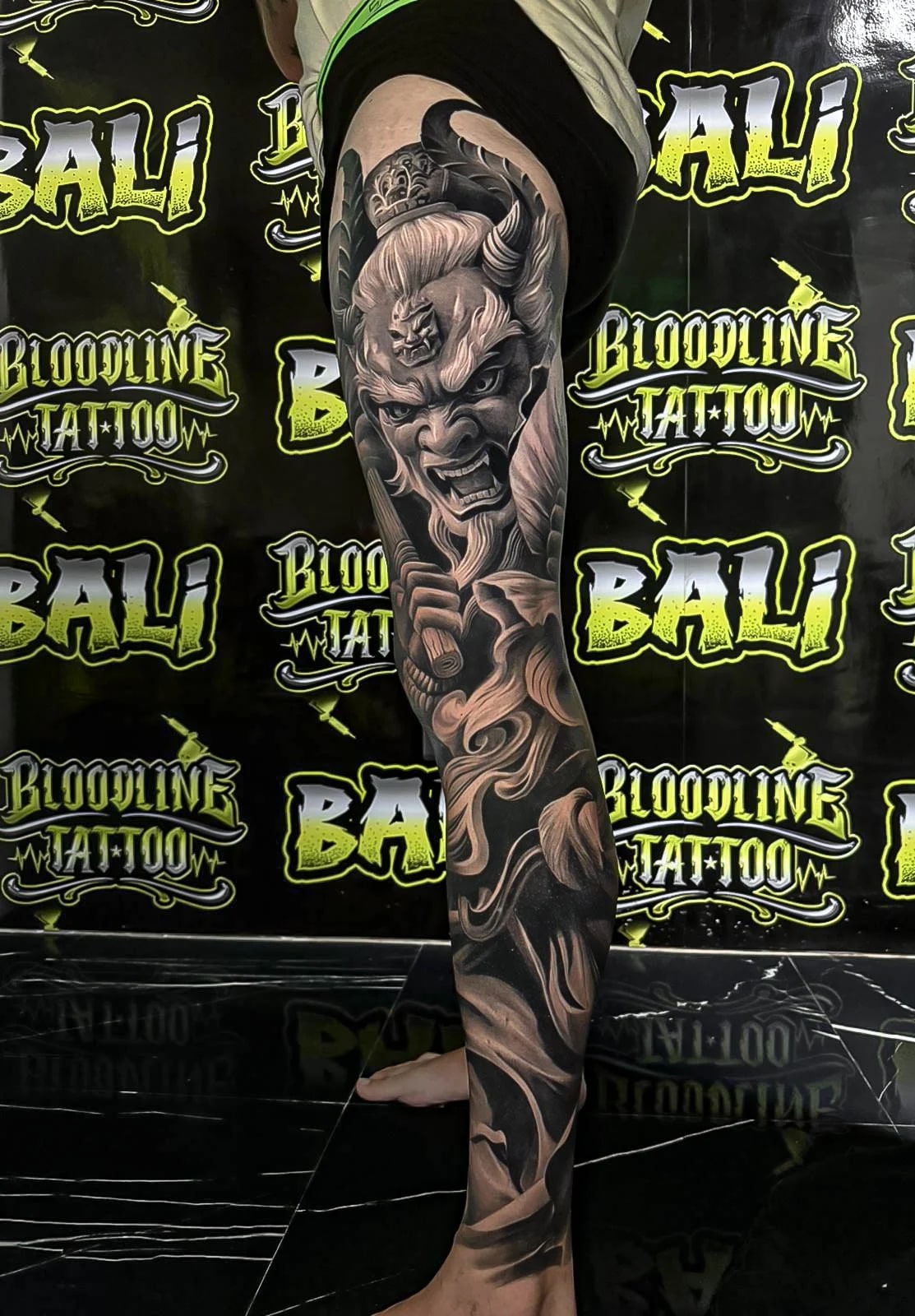 Healed black-and-grey leg sleeve with a horned Oni face and smoke-like hair flow, showing velvety shading and sharp healed line integrity at Bloodline Tattoo Bali.