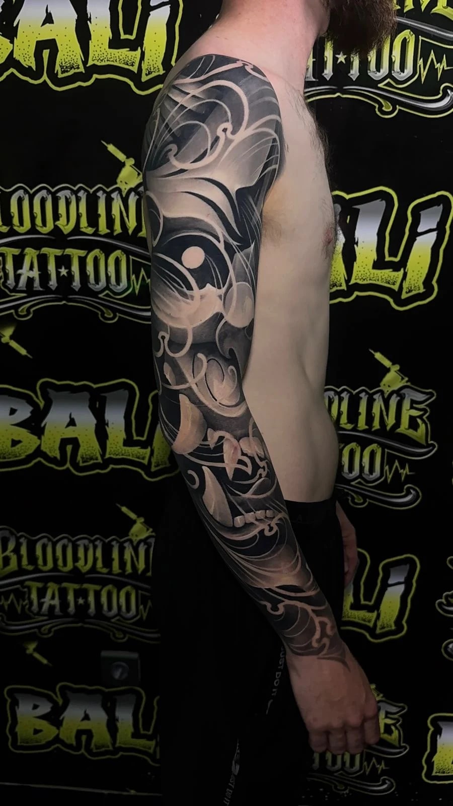 Healed abstract black-and-grey full sleeve with flowing wave forms, orbital circles, and ornamental swirls, showing smooth healed saturation at Bloodline Tattoo Bali.