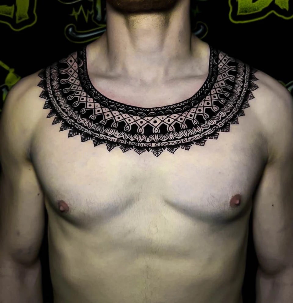Ornamental chest collar tattoo with lace-like mandala borders, micro dotwork detail, and necklace-style symmetry across the clavicles at Bloodline Tattoo Bali.