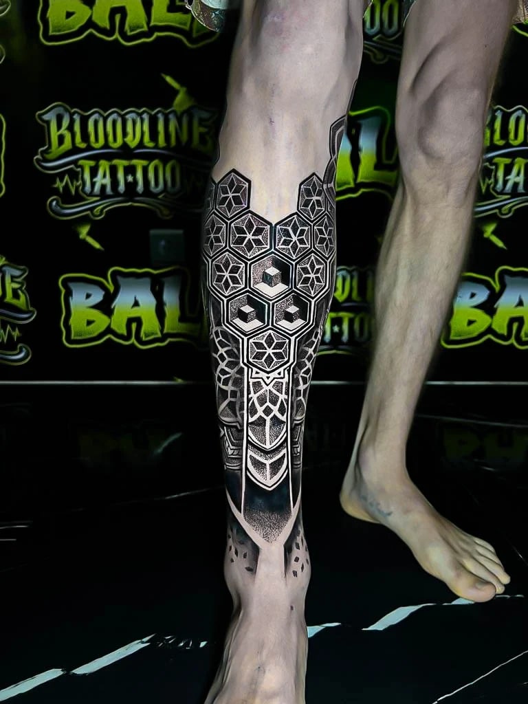 Geometric shin piece with hexagon rosettes, cube accents, and stippled blackwork packed into a symmetrical lower-leg panel at Bloodline Tattoo Bali.