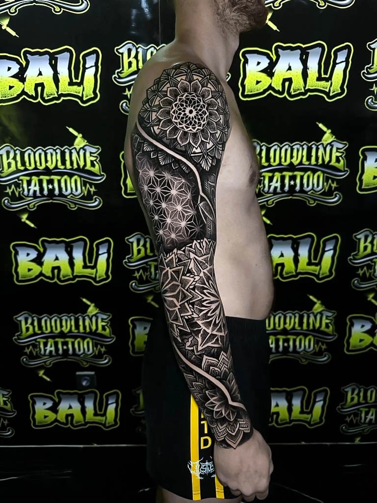 Full sleeve with a shoulder lotus mandala, Flower of Life field, angular star geometry, and layered dotwork from upper arm to wrist at Bloodline Tattoo Bali.