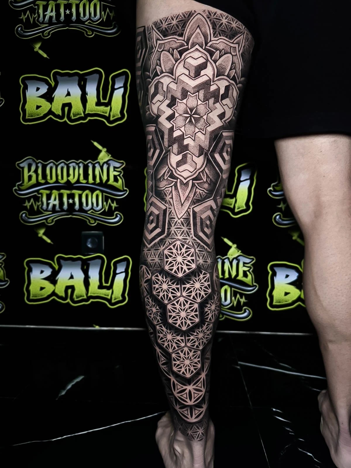 Sacred geometry calf piece with hexagon Flower of Life clusters, ornamental lotus framing, and 3D cube shading through the upper calf at Bloodline Tattoo Bali.