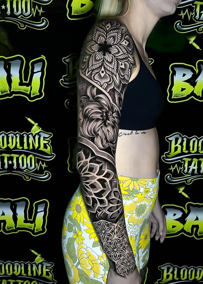 Floral black-and-grey sleeve with a shoulder mandala bloom, chrysanthemum center, and ornamental wrist rosettes balanced by negative space at Bloodline Tattoo Bali.