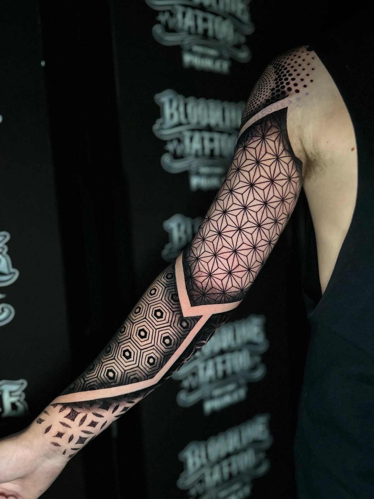 Geometric mandala sleeve with Asanoha triangle upper arm panels, a bold elbow band, and concentric 3D-shaded hexagons on the forearm at Bloodline Tattoo Phuket.