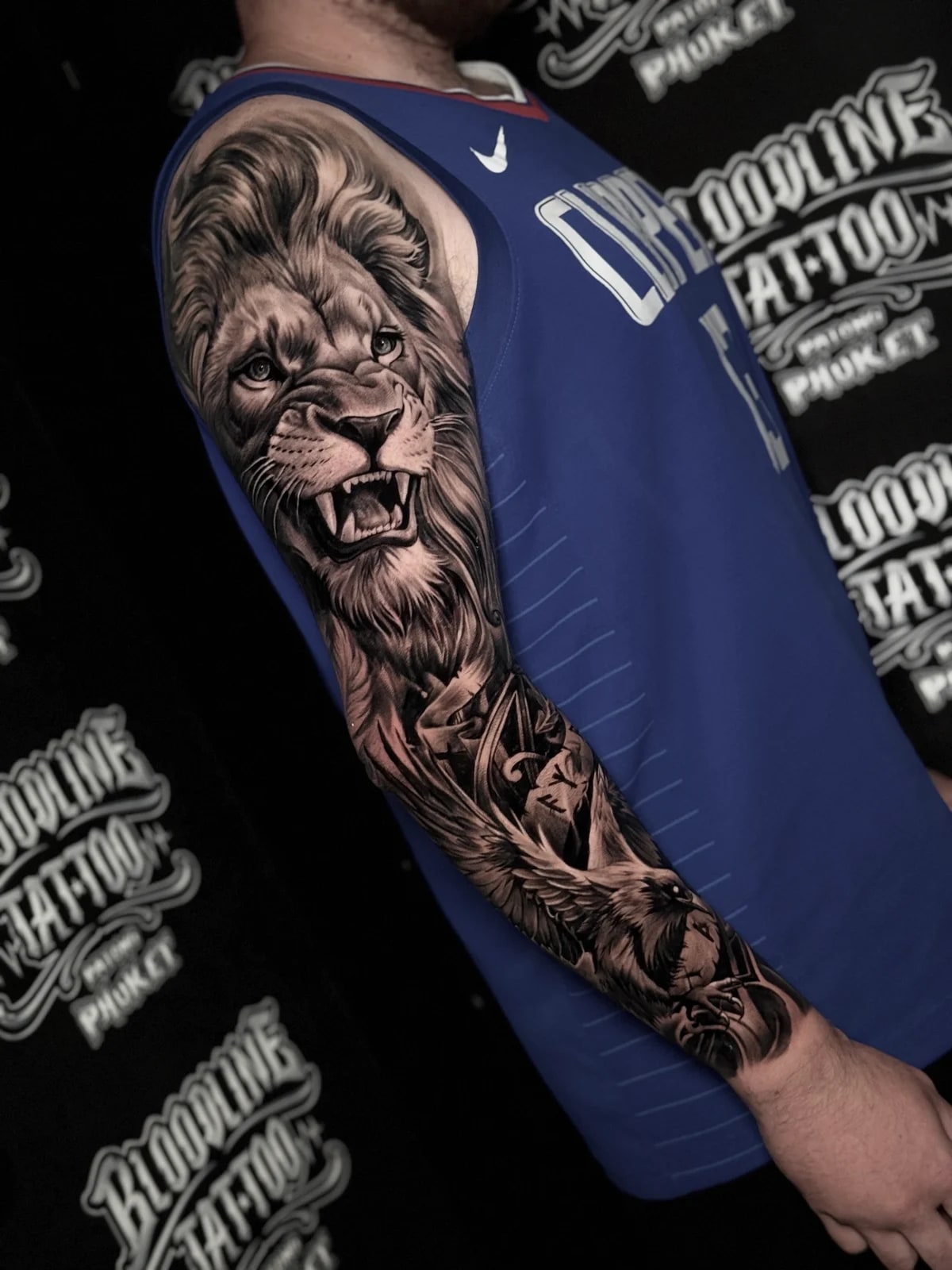 Detailed black and grey realism tattoo sleeve featuring a snarling lion on the upper arm and an eagle with spread wings on the forearm at Bloodline Tattoo Phuket.