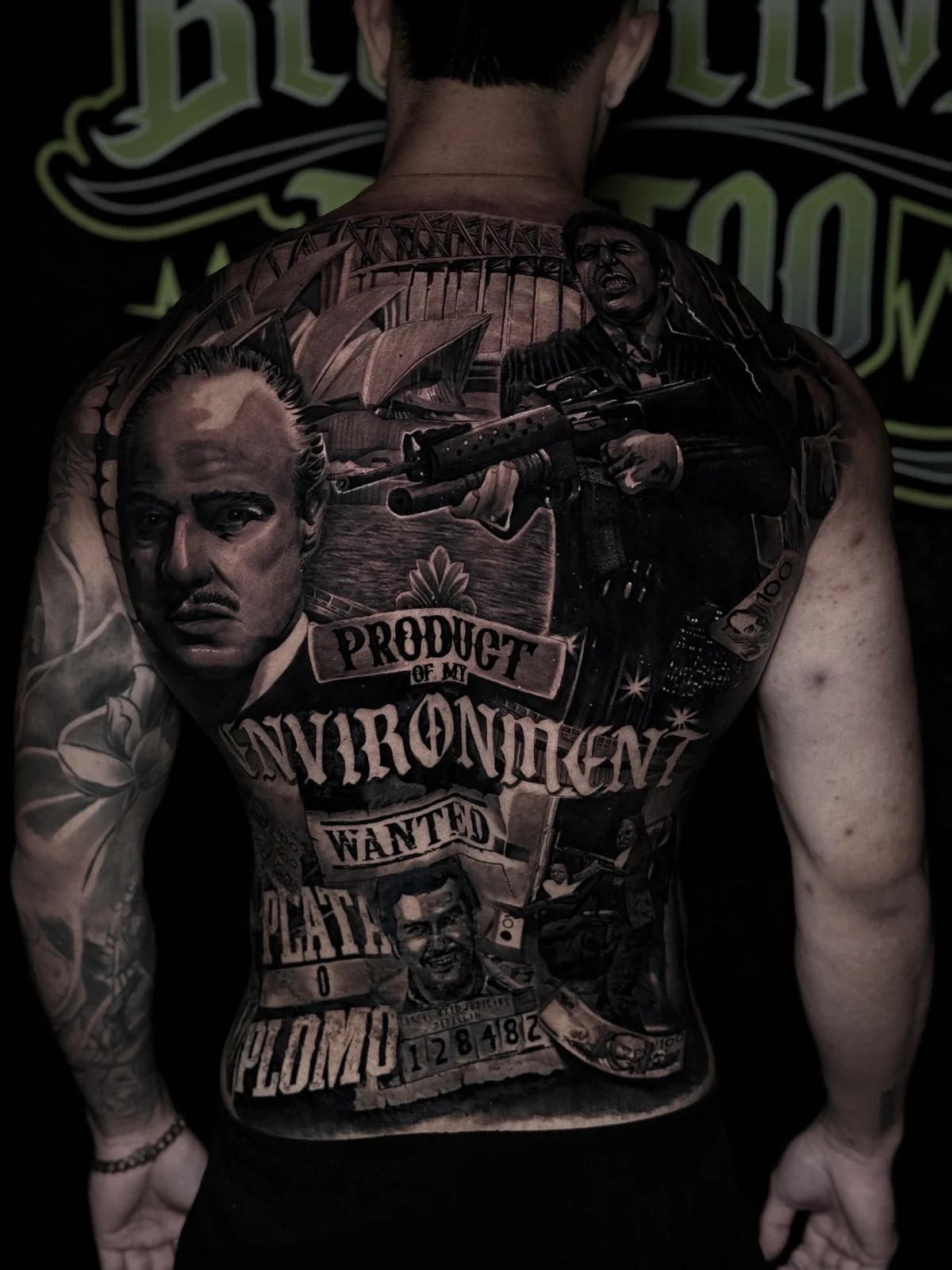 Detailed black and grey realism full back tattoo featuring The Godfather, Sydney Opera House, Tony Montana, Pablo Escobar mugshot, and Product of My Environment banner at Bloodline Tattoo Phuket.